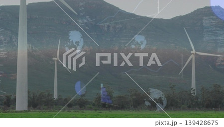 Towering wind turbines rotating across grassy pasture below mountain ridge, showing globe icons Towering wind turbines rotating across grassy pasture below mountain ridge, showing globe icons 139428675