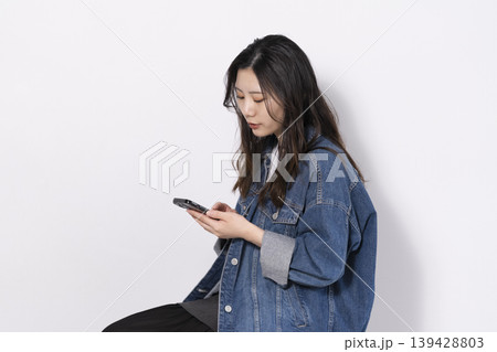 椅子に座って携帯電話を操作する若い女性 椅子に座って携帯電話を操作する若い女性 139428803