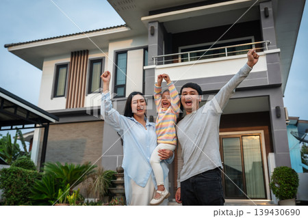 happy family, cheerful father and mother holding child girl with arm raised while standing in front of their house happy family, cheerful father and mother holding child girl with arm raised while standing in front of their house 139430690