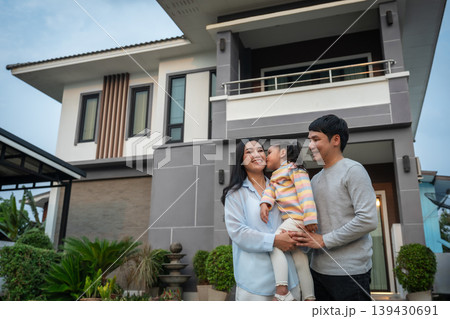 happy family, father and mother holding and kissing with child girl while standing in front of their house happy family, father and mother holding and kissing with child girl while standing in front of their house 139430691