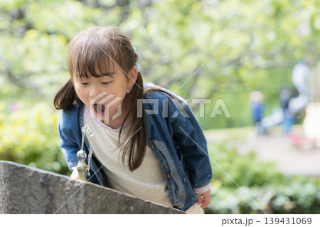 公園の水飲み場で水分補給する女の子のポートレート新緑と遊ぶ、暑い日のイメージ 139431069