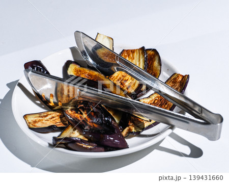 Grilled eggplant slices in a white bowl with metal tongs Grilled eggplant slices in a white bowl with metal tongs 139431660