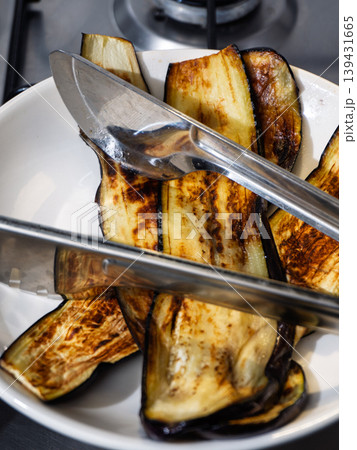 Grilled eggplant slices in a white bowl with stainless steel tongs Grilled eggplant slices in a white bowl with stainless steel tongs 139431665