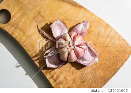 Opened purple garlic bulb arranged on a wooden cutting board 139431666