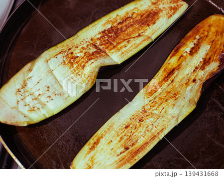 Two long eggplant slices frying in a dark pan until golden brown Two long eggplant slices frying in a dark pan until golden brown 139431668