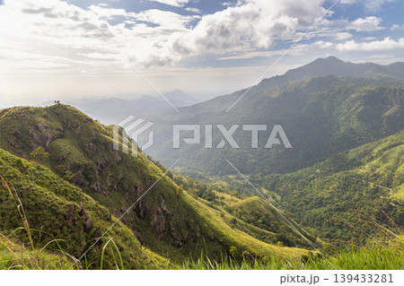 Dramatic Mountain Landscape View with Lush Green Slopes and Distant Peaks Under a Cloudy Sky at Golden Hour. View from Little Adam's Peak in Sri Lanka. 139433281