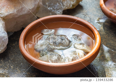 Gemstones in Sri Lanka. Close up of small, natural, light-colored stones submerged in clear water within a rustic, round terracotta bowl, creating a serene and zen-like display. Gemstones in Sri Lanka. Close up of small, natural, light-colored stones submerged in clear water within a rustic, round terracotta bowl, creating a serene and zen-like display. 139433286