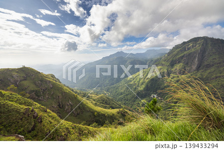 Breathtaking Mountainous Landscape with Lush Green Valleys Under a Dramatic Sky, Serene Scenic Vista. View from Little Adam's Peak in Sri Lanka. Breathtaking Mountainous Landscape with Lush Green Valleys Under a Dramatic Sky, Serene Scenic Vista. View from Little Adam's Peak in Sri Lanka. 139433294