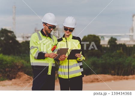 Petroleum specialists analyzing data from tablet during field operation near oil refinery Petroleum specialists analyzing data from tablet during field operation near oil refinery 139434368