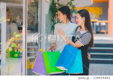 Two women are shopping in a store and pointing at the bags they are holding 139434401