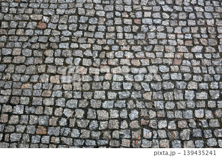 Cobblestone pavement surface with irregularly shaped stones in various shades of gray and brown, creating a textured and durable walking area Cobblestone pavement surface with irregularly shaped stones in various shades of gray and brown, creating a textured and durable walking area 139435241