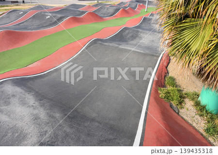 Empty coastal pump track with undulating asphalt waves and colorful lanes near marina for biking and skate sports Empty coastal pump track with undulating asphalt waves and colorful lanes near marina for biking and skate sports 139435318