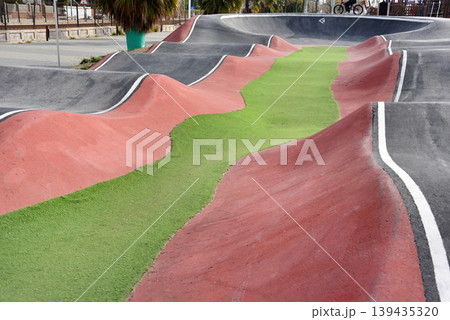Empty coastal pump track with undulating asphalt waves and colorful lanes near marina for biking and skate sports 139435320