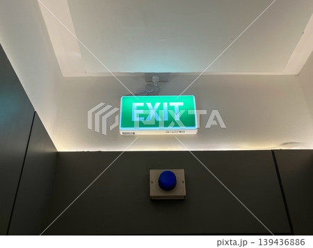 Green emergency exit sign glowing above the door in a dark office building hallway. Safety symbol for evacuation route, fire exit guidance, and concept of finding a way out or solution Green emergency exit sign glowing above the door in a dark office building hallway. Safety symbol for evacuation route, fire exit guidance, and concept of finding a way out or solution 139436886