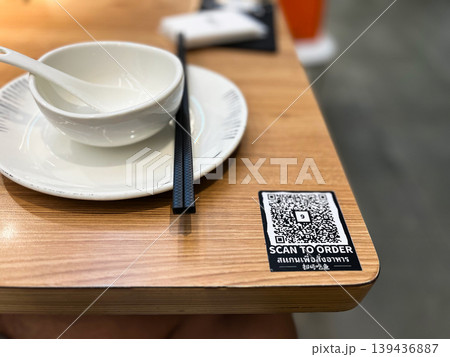 QR code on wooden restaurant table for digital menu and scan to order service. Modern contactless dining technology with white ceramic bowl and chopsticks in blurred background setting QR code on wooden restaurant table for digital menu and scan to order service. Modern contactless dining technology with white ceramic bowl and chopsticks in blurred background setting 139436887
