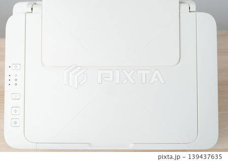Multifunction printer and scanner photographed from above on a wooden desk, showcasing a clean minimal office workspace with control buttons, paper drawer and neutral tones for business and home use. 139437635