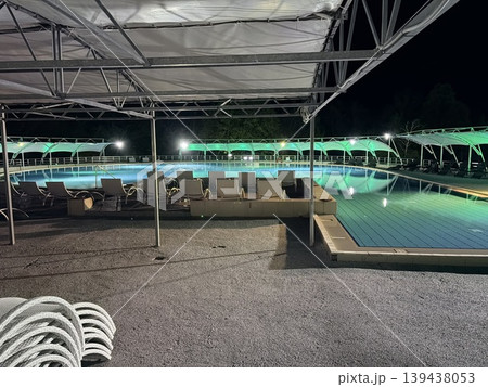 A tranquil swimming pool complex at night, illuminated by artificial lighting. 139438053