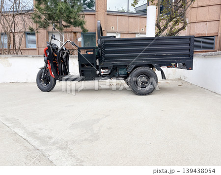 A three-wheeled electric cargo truck parked on a light-gray concrete surface. 139438054