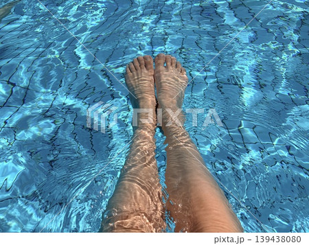 A pair of legs and feet submerged in the shimmering blue water of a swimming pool. 139438080