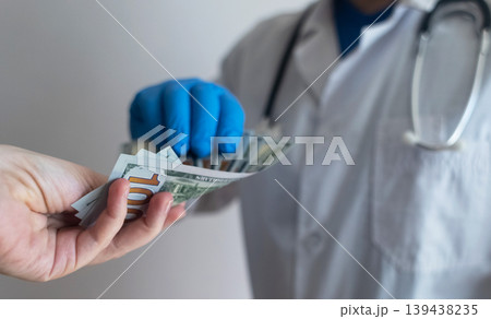 Close-up of doctor in white coat and blue gloves receiving or hiding cash. Concept of high medical salary, corruption in medicine, healthcare bribery, and expensive health insurance. Close-up of doctor in white coat and blue gloves receiving or hiding cash. Concept of high medical salary, corruption in medicine, healthcare bribery, and expensive health insurance. 139438235