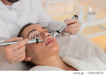 Caucasian young woman gets lips zone facial therapy with modern device by cosmetologist in clinic 139439558