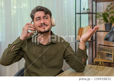 Middle-aged man removes headphones sighs upset by bad audio feeling sad and frustrated at table desk 139439632