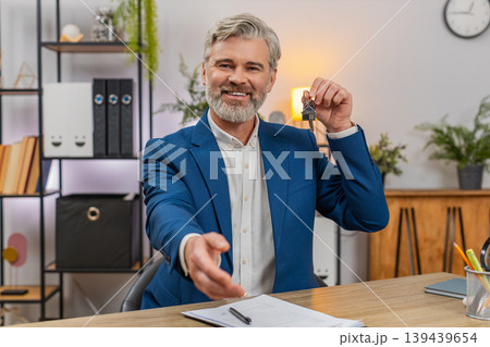 Middle-aged businessman signs lease holds apartment keys smiles shakes agent hand marking milestone Middle-aged businessman signs lease holds apartment keys smiles shakes agent hand marking milestone 139439654