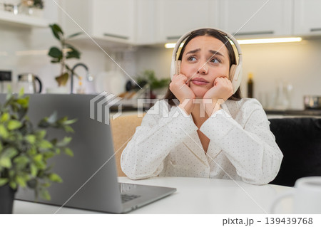 Young woman in headphones thinking with laptop leans on hands worried decision responsibility mind 139439768