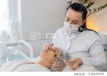 Enzyme therapy, beautician applying moisturizing medical cream on young woman face with brush Enzyme therapy, beautician applying moisturizing medical cream on young woman face with brush 139439797
