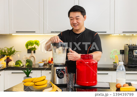 Asian man using blender to mix banana milk cottage cheese whey protein shake in home kitchen daily Asian man using blender to mix banana milk cottage cheese whey protein shake in home kitchen daily 139439799