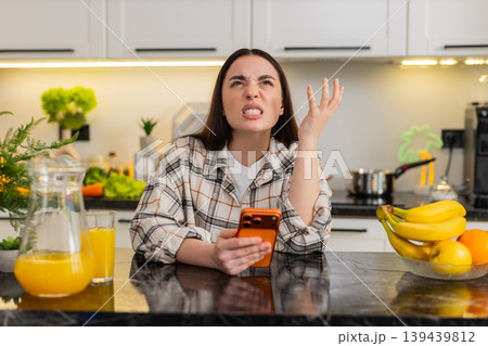 Young woman upset after losing online casino game on orange smartphone at kitchen table at home solo Young woman upset after losing online casino game on orange smartphone at kitchen table at home solo 139439812