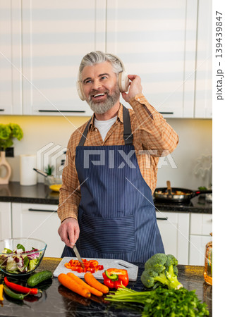 Middle-aged man chopping red pepper wearing headphones enjoying music while preparing healthy meal 139439847
