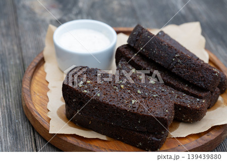 Black garlic bread appetizer with white sauce on a wooden board. 139439880