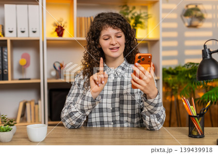 Young woman on home table talking on smartphone and explaining important details during video call 139439918