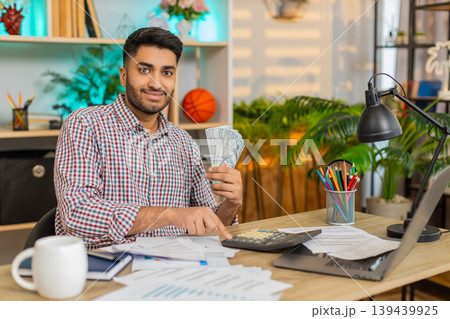 Indian man on home table counting cash with calculator while planning family budget and big expenses Indian man on home table counting cash with calculator while planning family budget and big expenses 139439925