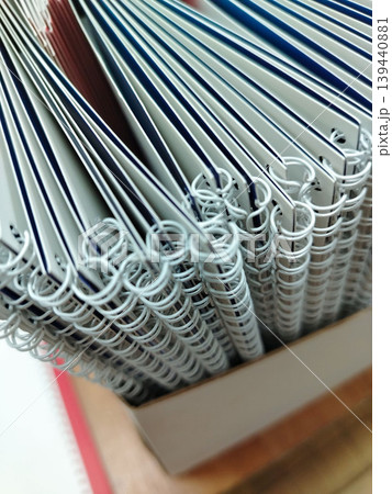 Stack of spiral-bound notebooks with white covers and colorful edges arranged neatly in a cardboard box on a wooden surface 139440881