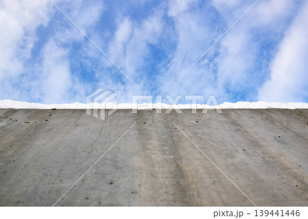 Blue sky with clouds visible from the top of a concrete surface under daylight. The scene shows textures of concrete and sky 139441446