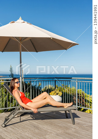 Woman sunbathing on veranda with ocean view Woman sunbathing on veranda with ocean view 139441991