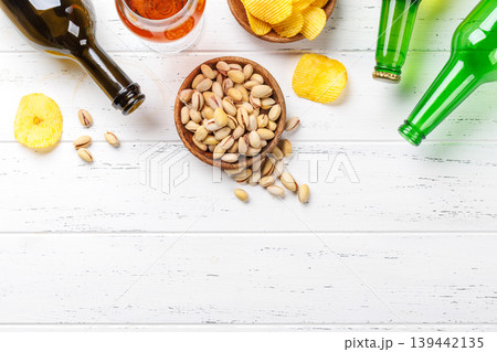 Beer bottles with pistachios and chips on white table Beer bottles with pistachios and chips on white table 139442135