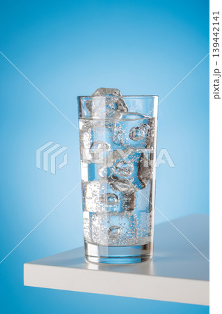 Glass of sparkling water with ice cubes on blue background minimal Glass of sparkling water with ice cubes on blue background minimal 139442141