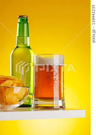 Beer mug with foam chips and bottle on yellow background snack setup Beer mug with foam chips and bottle on yellow background snack setup 139442235