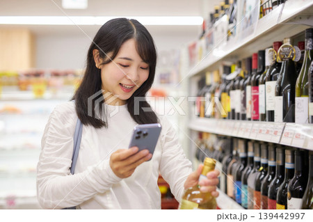 スーパーマーケットでスマホメモを見ながら買い物をする若い女性 139442997