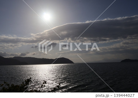 白く輝く太陽と雲と青空とシルエットの山と湖面と光る水面の琵琶湖の朝の風景 白く輝く太陽と雲と青空とシルエットの山と湖面と光る水面の琵琶湖の朝の風景 139444027