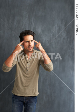 Annoyed, thinking and portrait of man by a wall with doubt, moody and angry facial expression. Upset, question and young male person from Canada with confused face pointing to head by gray background 139445444