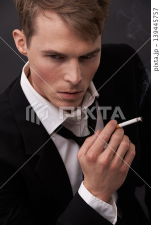 Face, thinking and a man smoking a cigarette in studio on a dark background for tobacco addiction. Nicotine, habit and unhealthy with a young person in a suit, taking a break from business to smoke 139445757
