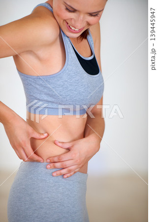 Fitness, stomach and woman holding skin for health, wellness and weight loss goals in a training studio. Smile, happy and young female person athlete showing body for exercise or workout at gym. Fitness, stomach and woman holding skin for health, wellness and weight loss goals in a training studio. Smile, happy and young female person athlete showing body for exercise or workout at gym. 139445947