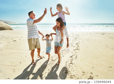 Parents, children and beach for high five in summer for travel vacation, ocean sunshine or sibling development. Man, woman and kids on sand for holiday relax walking or outdoor, clean air or smile Parents, children and beach for high five in summer for travel vacation, ocean sunshine or sibling development. Man, woman and kids on sand for holiday relax walking or outdoor, clean air or smile 139446044