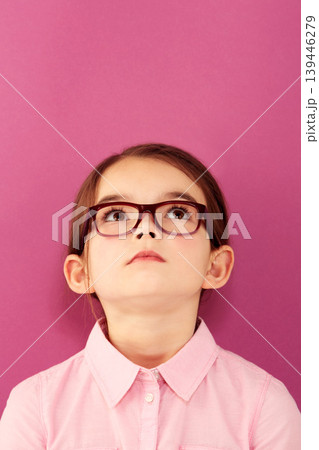 Glasses, child and looking up with thinking geek and modern fashion in a studio with serious face. Kid, eyewear and sight with outfit and nerd with accessory and pink background with confidence 139446279