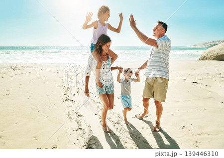 Parents, children and beach for high five happy or summer travel vacation, ocean sunshine or family development. Man, woman and kids on sand for holiday relax walking or outdoor, clean air or smile 139446310