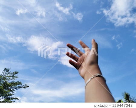 A hand in front of beautiful blue sky with white cumulus clouds A hand in front of beautiful blue sky with white cumulus clouds 139447048
